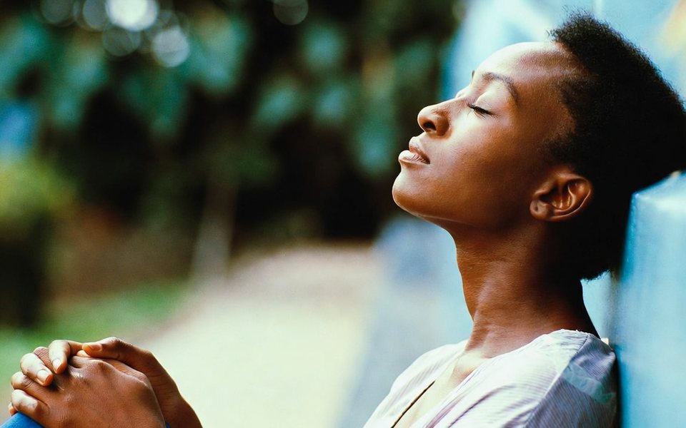 A woman with her eyes closed, resting for a moment against a wall outdoors.